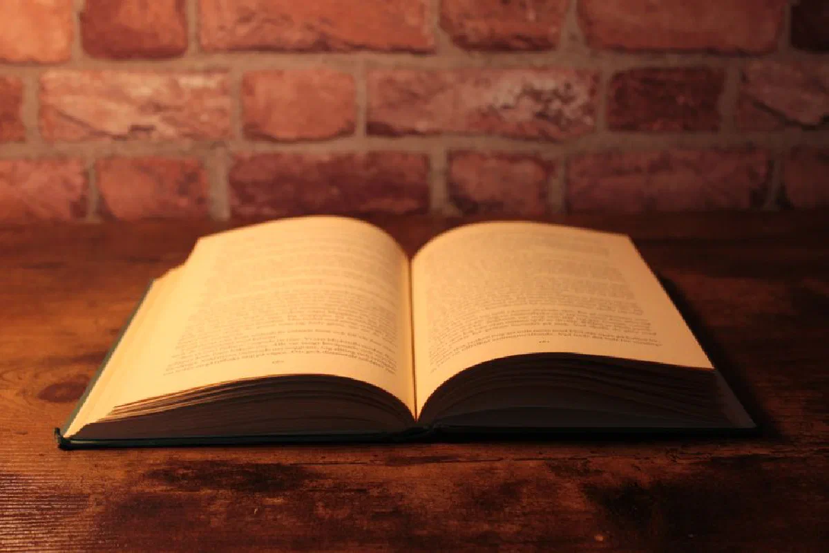 An open book resting on a wooden table against a rustic brick wall, ideal for reading concepts.