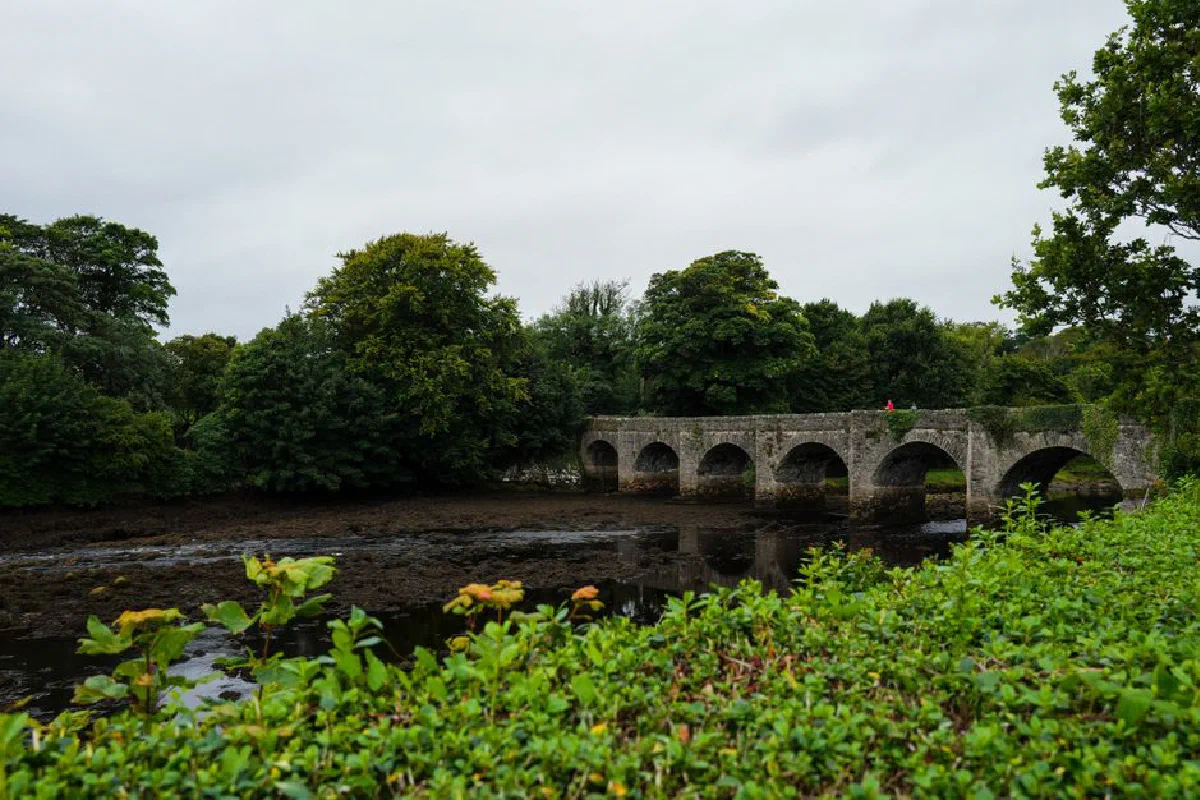 Scenic view of old stone arch bridge crossing a tranquil river surrounded by lush greenery.
