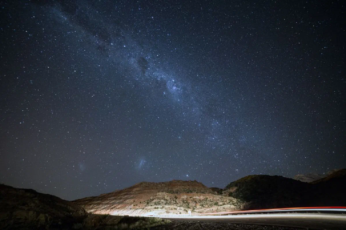 Stunning long exposure of a starry night sky over the Mendoza mountains with light trails on a road.