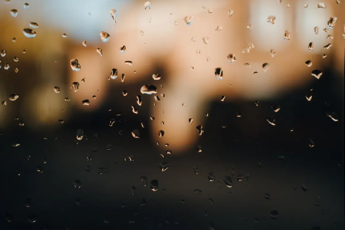 Closeup of chaotic rain drops on transparent glass window at sunset as abstract background