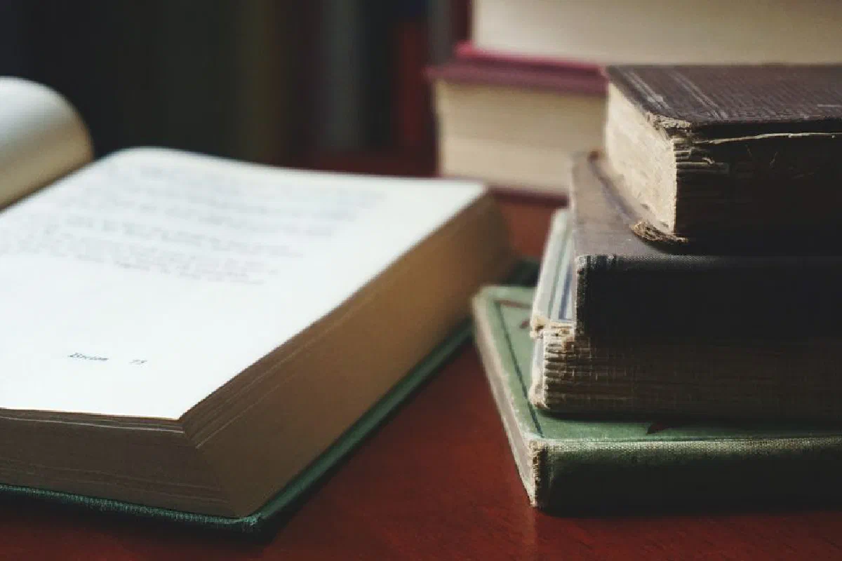 A collection of aged books stacked neatly on a wooden table for reading enthusiasts.