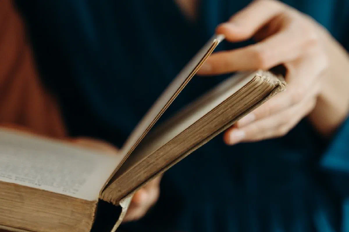 Person holding and flipping through pages of an old book.