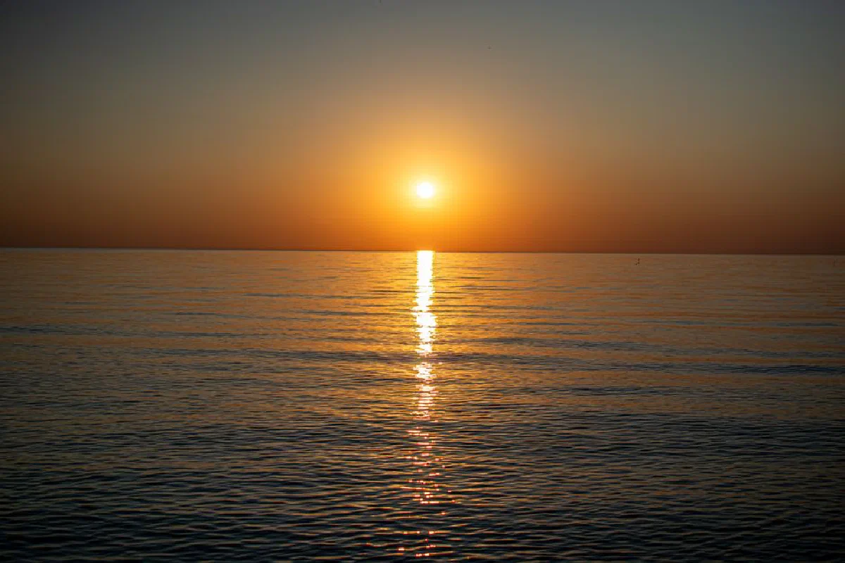 A tranquil sunset with golden reflections on the ocean's smooth surface, capturing a peaceful moment.