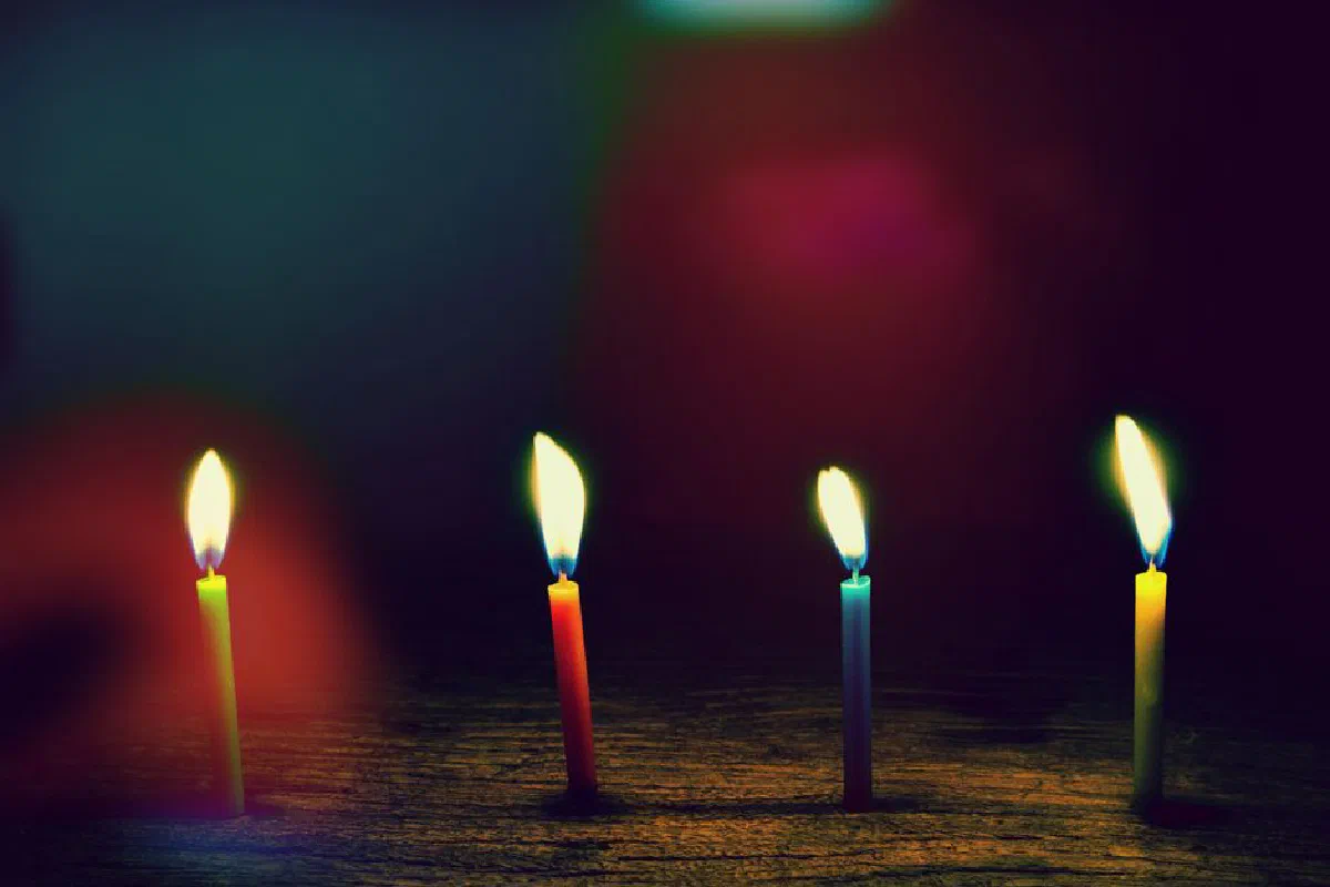 A serene view of four colorful candles burning quietly in the dark.