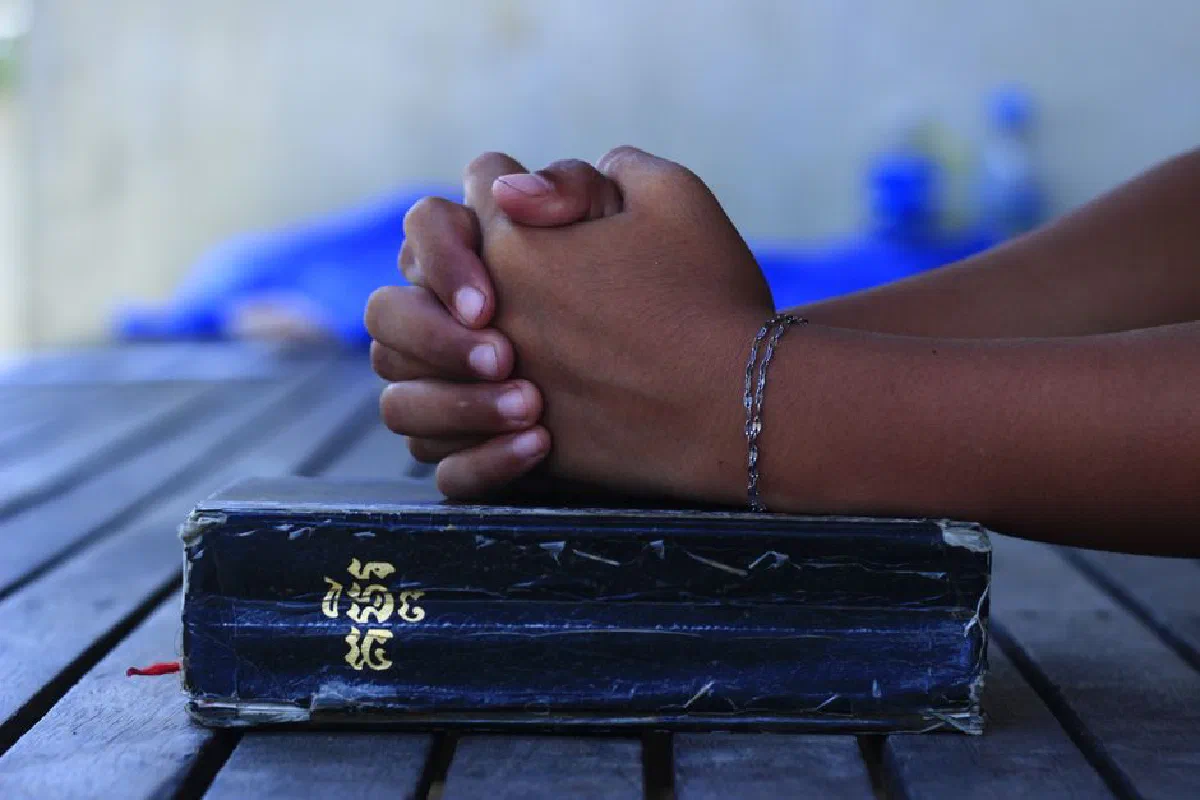 A close-up of hands clasped over a book on a wooden table, captured in Cambodia.
