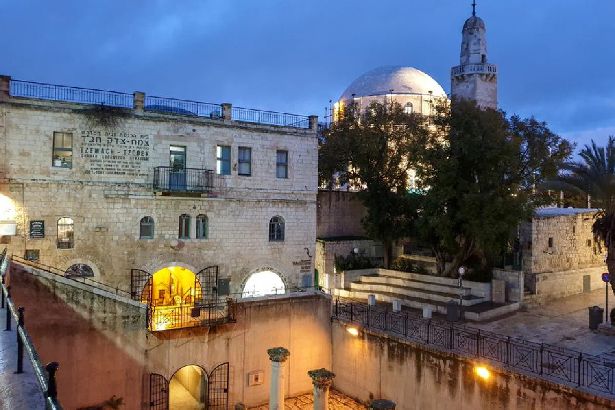 Illuminated Hurva Synagogue in Jerusalem's Old City under a vivid blue sky at dusk.