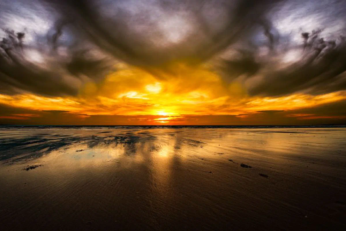 Vibrant sunset over an empty beach with reflection and dramatic clouds enhancing the serene scene.