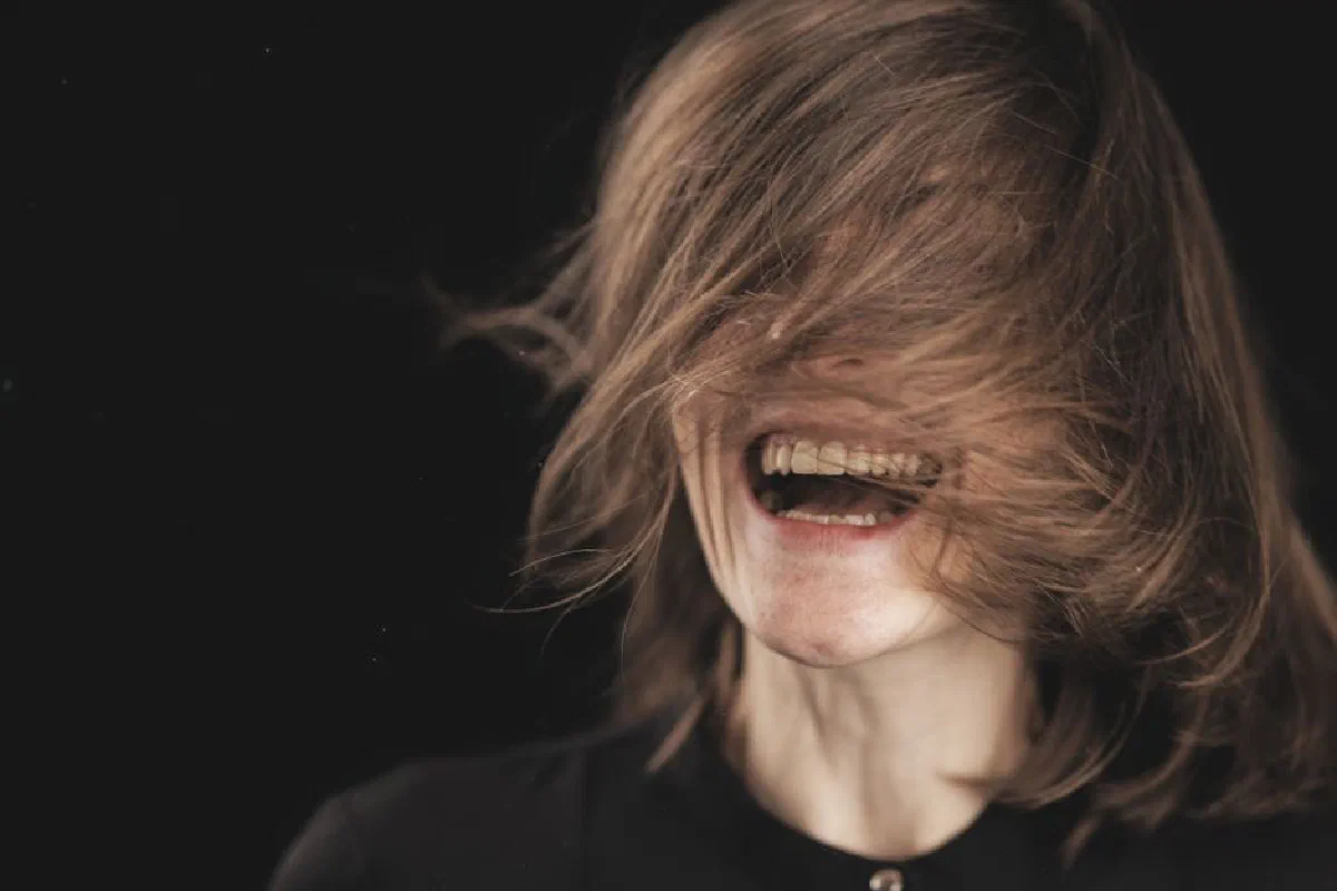 A woman joyfully laughing with her hair covering her face against a black background.