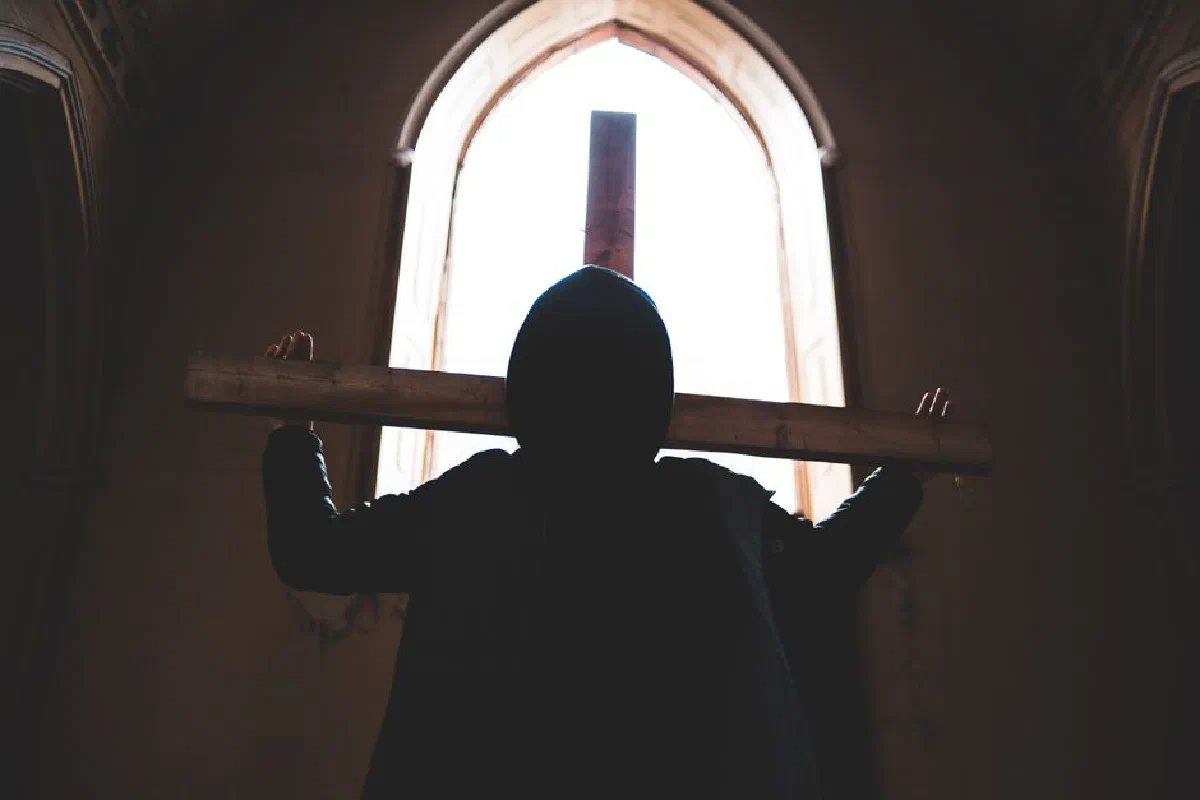 Silhouette of a man with a wooden cross inside a dimly lit church.