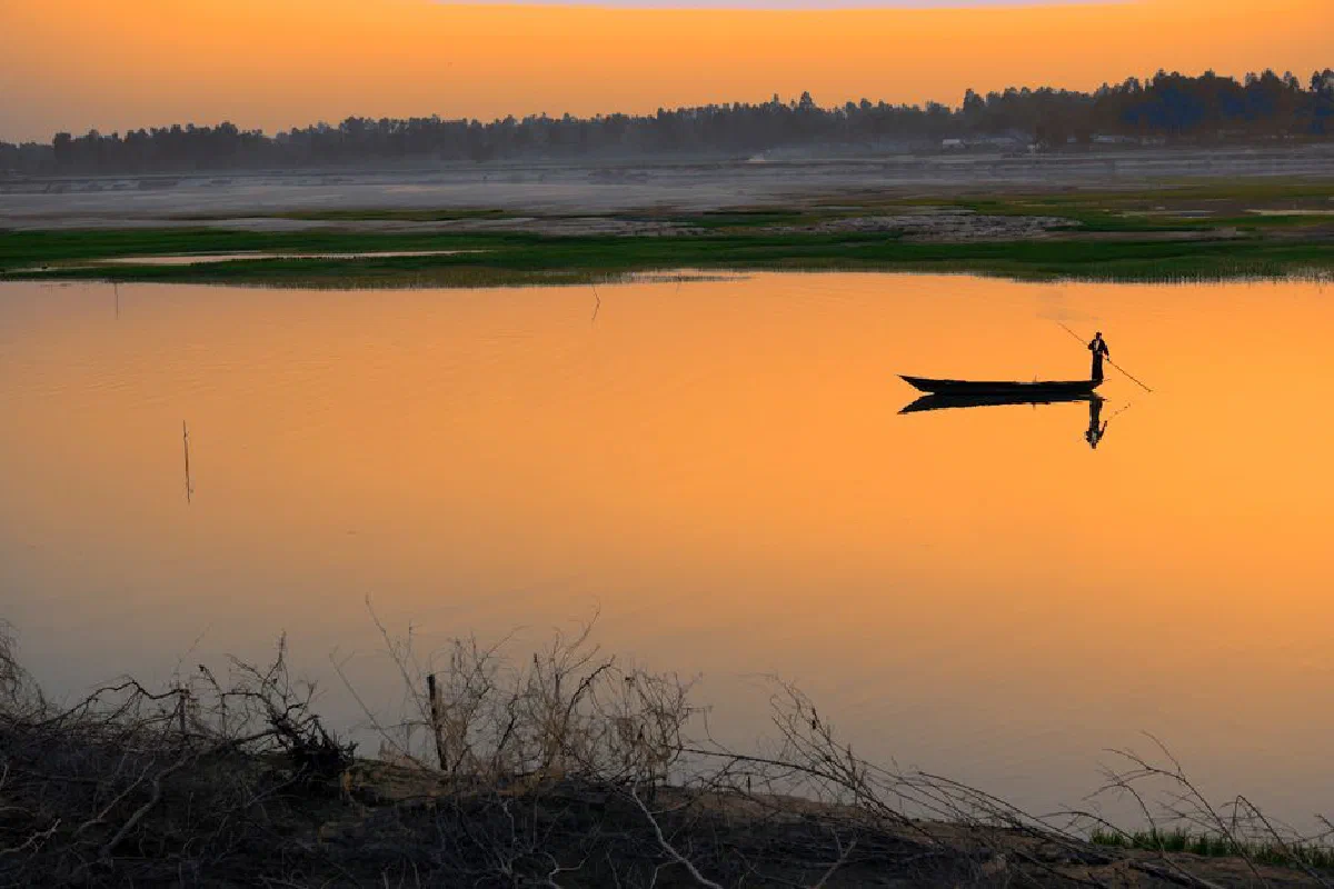 A lone boatman glides at sunset, casting a serene reflection on tranquil waters.