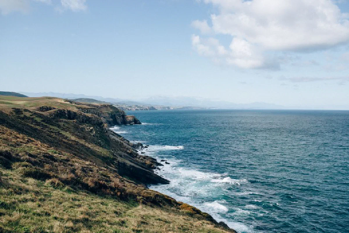 Scenic coastal cliffs with waves crashing under a clear blue sky, depicting natural beauty.