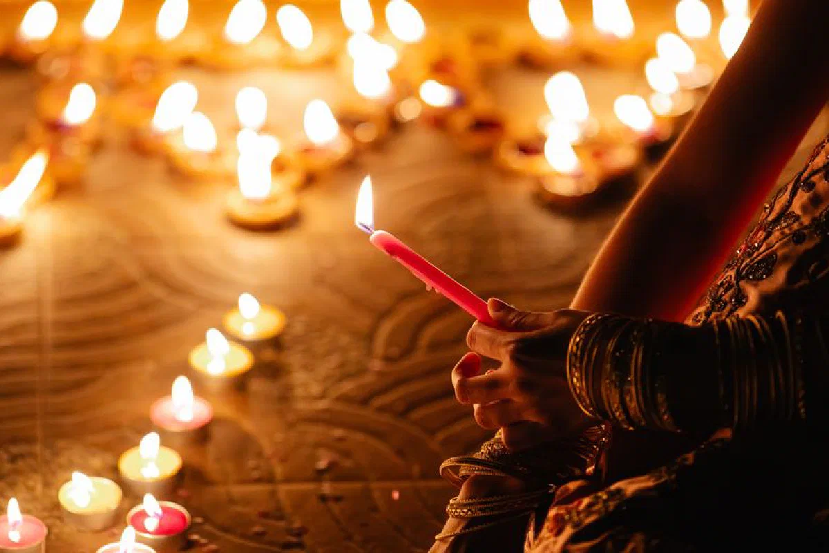 A close-up of hands holding a candle during a Diwali festival, surrounded by glowing candles.