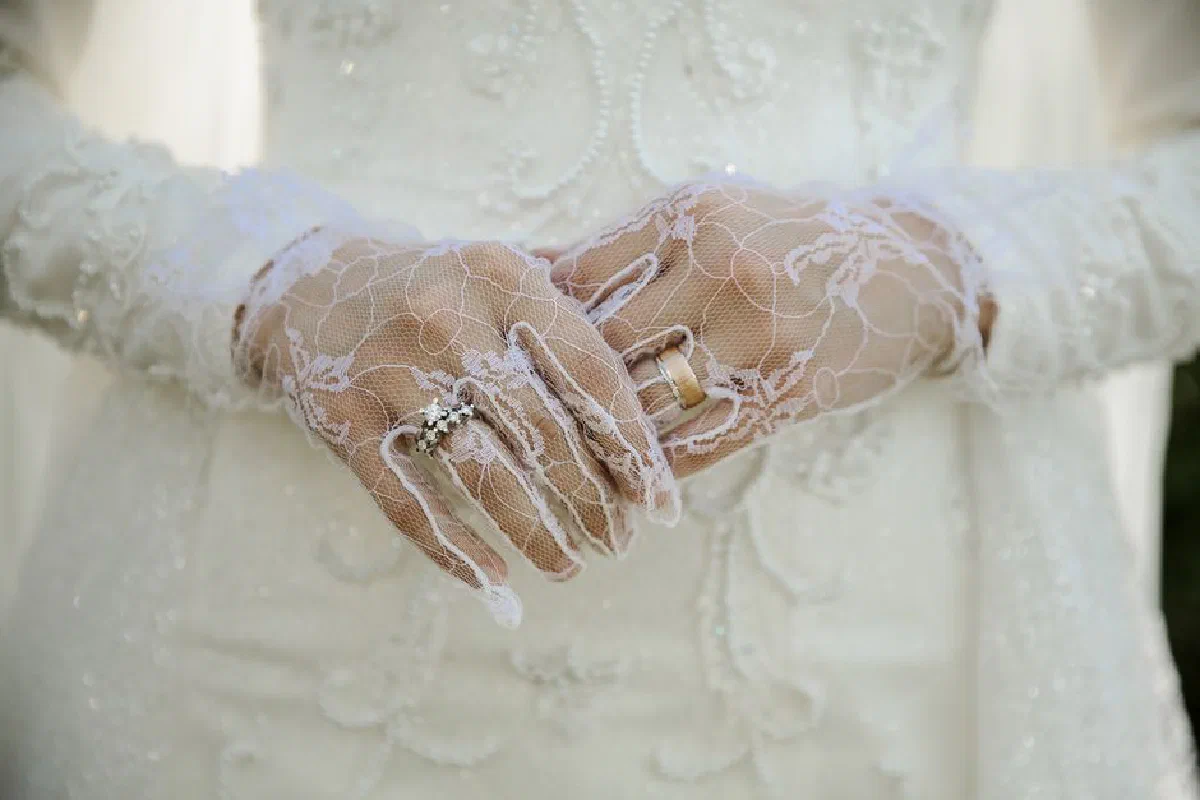 Close-up of elegant bridal gloves and wedding rings on a lace wedding dress.