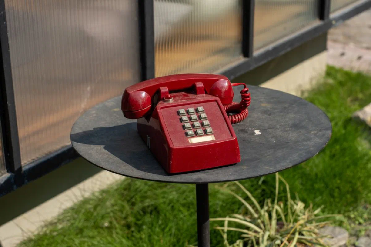 Classic red rotary telephone placed outdoors on a metal table.