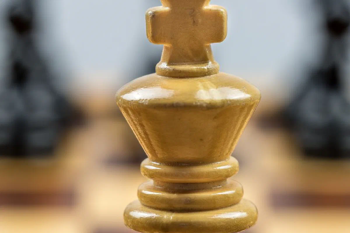 Detailed view of a wooden chess king piece on a chessboard with blurred pieces in the background.