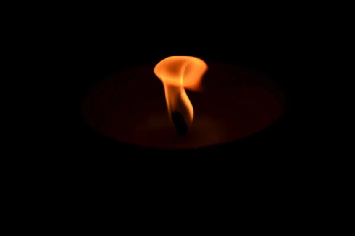 A close-up image of a candle flame glowing in darkness, creating a warm and serene atmosphere.