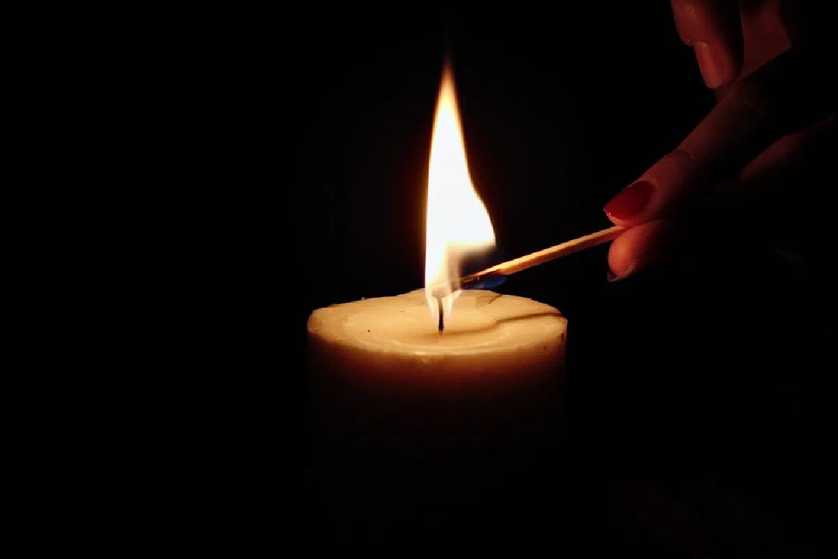 Close-up of a candle being lit by hand with a match in a dark setting.