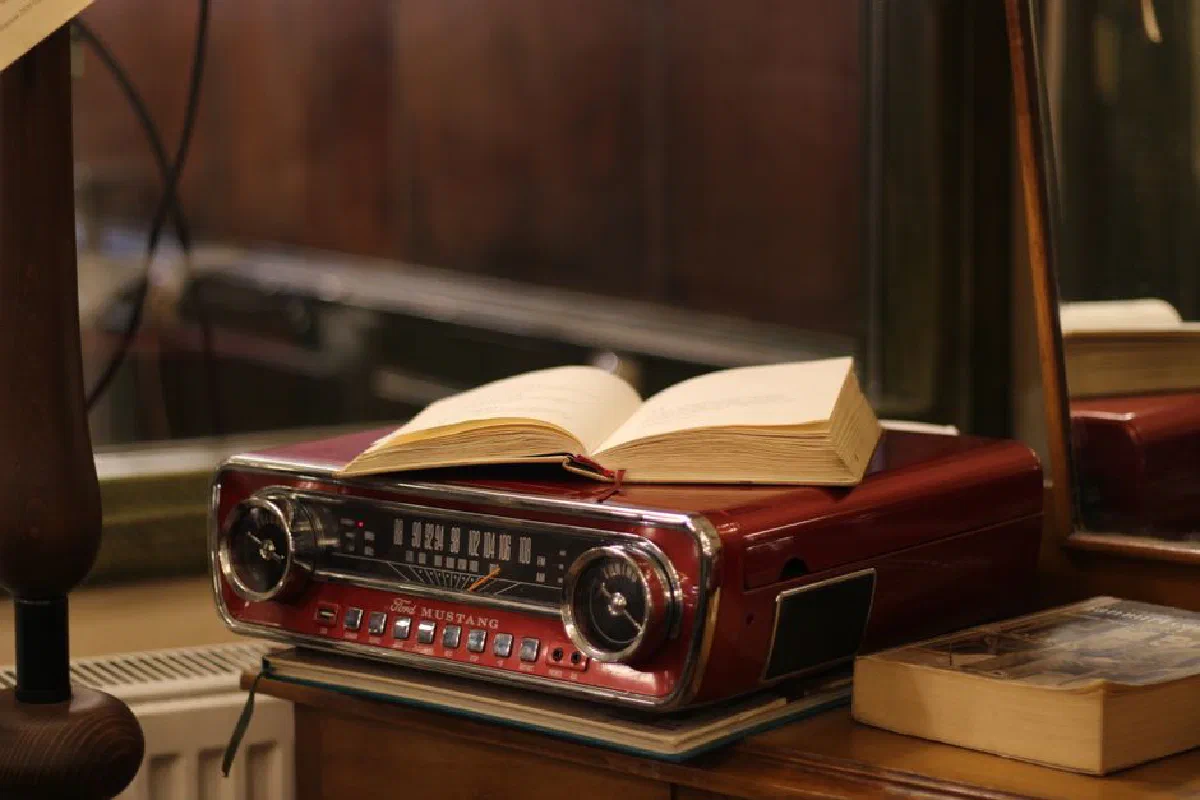 A vintage red Ford Mustang radio with an open book on a wooden desk, indoors.