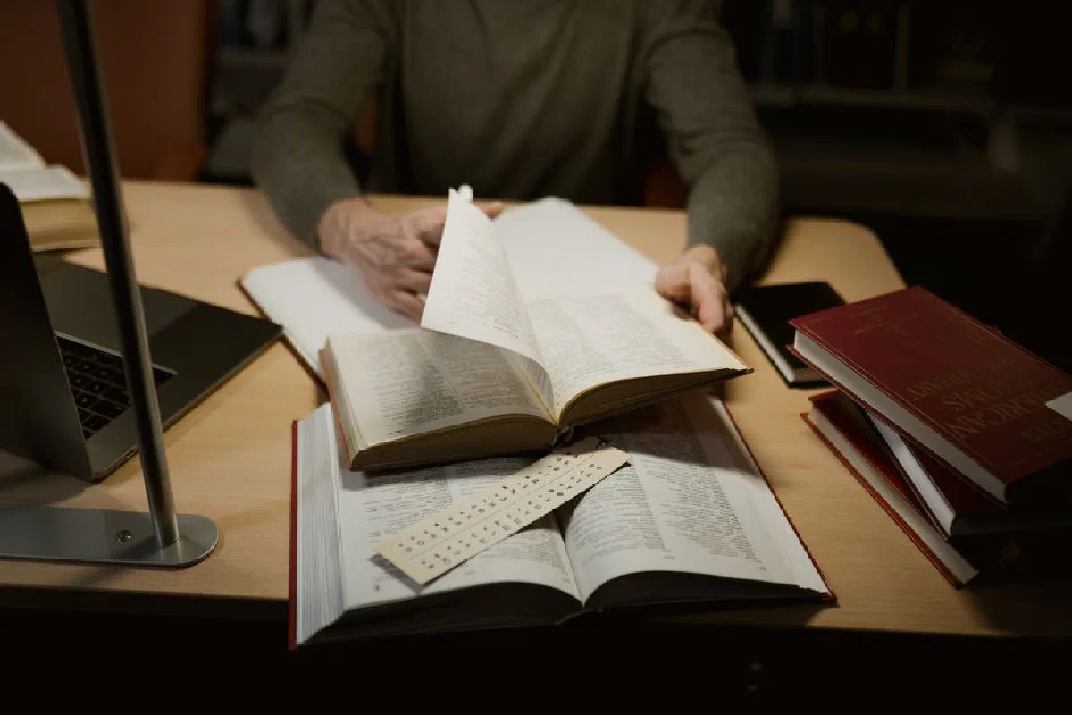 A person engrossed in studying with open books on a desk.
