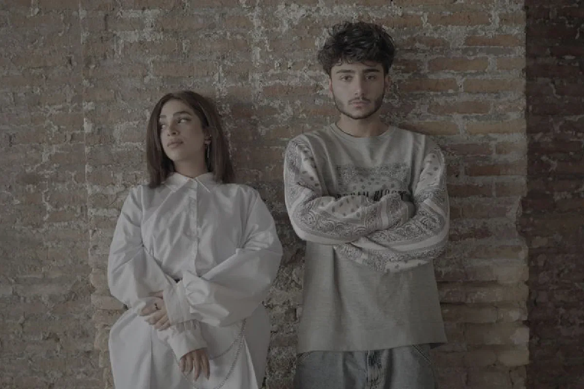 Young man and woman standing against a rustic brick wall, showcasing modern fashion and style.