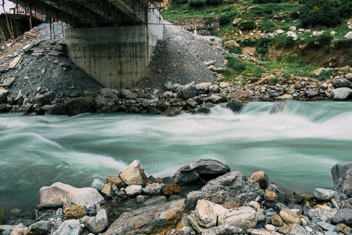 Mountain river flowing under a bridge with rocks and greenery, showcasing natural beauty.