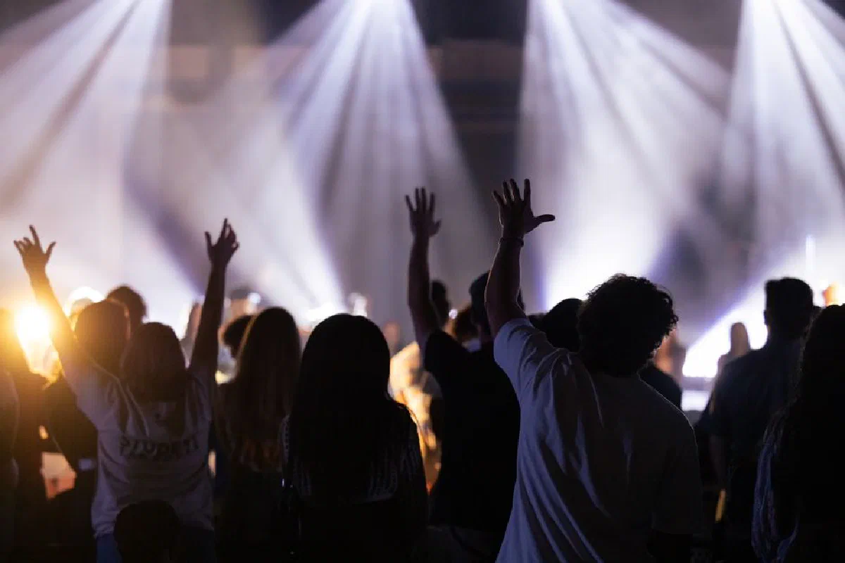 Silhouette of a crowd with raised hands enjoying a worship concert with bright stage lights.