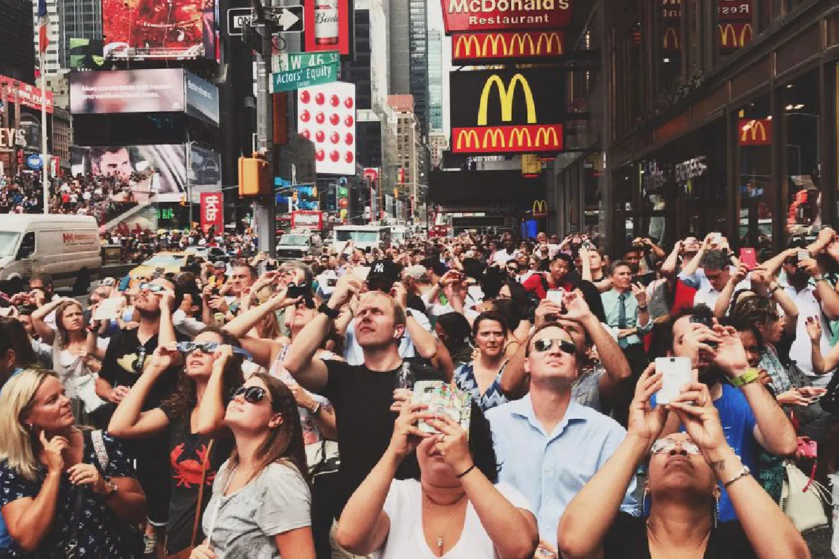 Diverse crowd in Times Square, New York City capturing moments with smartphones.
