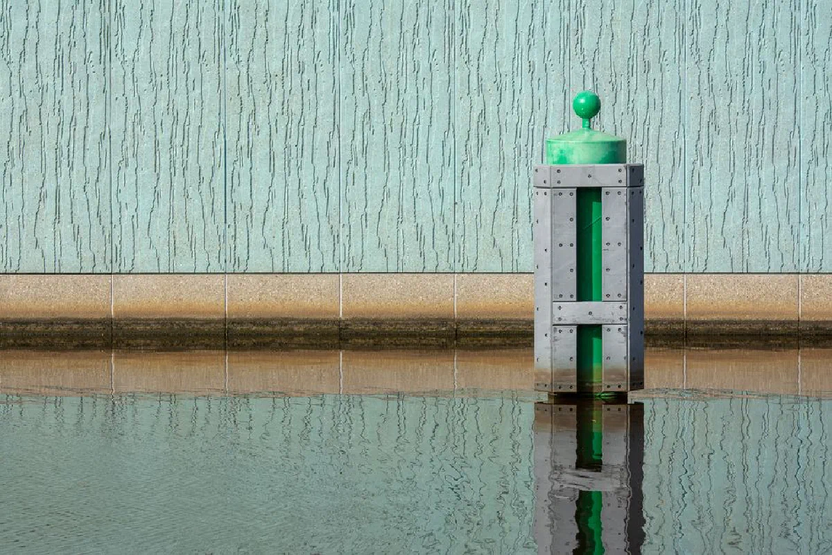 Green buoy reflected in calm water, set against a textured wall, creating a minimalist aquatic scene.