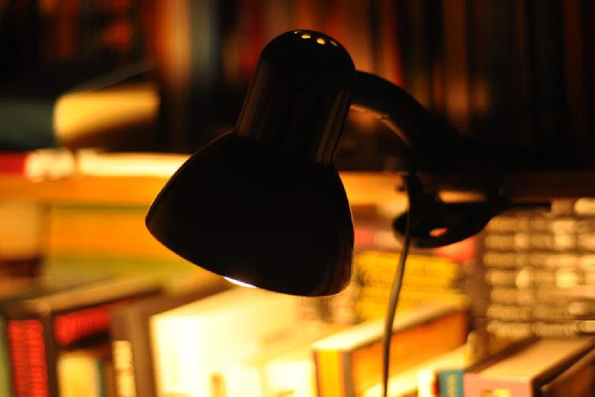 A close-up of a desk lamp casting a warm glow over books in a dimly lit library.