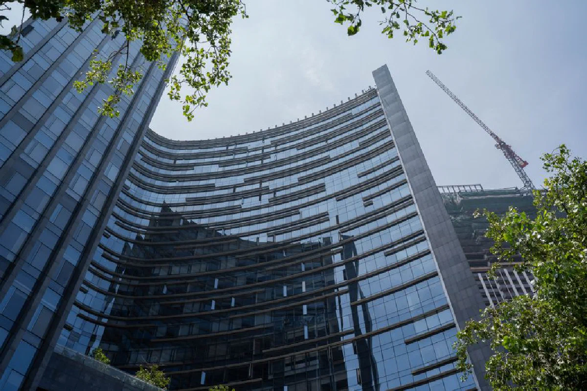 A modern glass skyscraper under construction with visible crane against a clear sky.