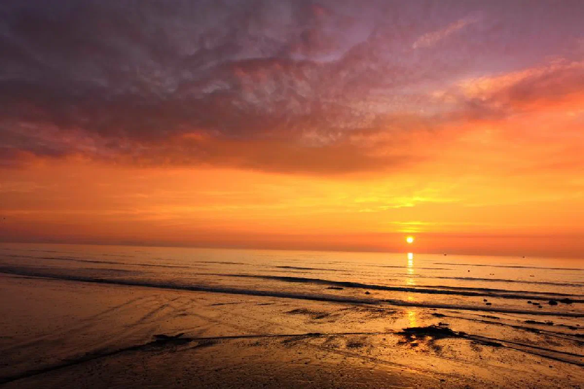 A stunning sunset casts vibrant colors over a serene beach and ocean waves.
