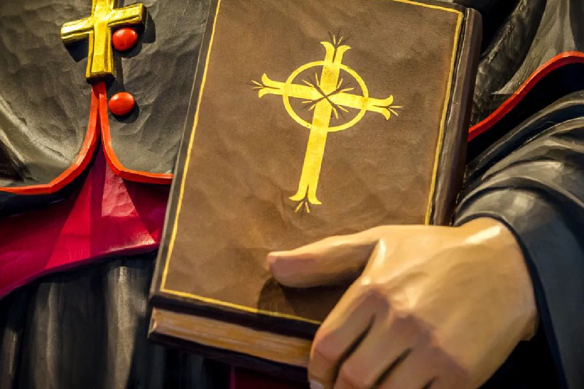 A close-up of a religious book with a cross held by a statue, symbolizing faith and spirituality.