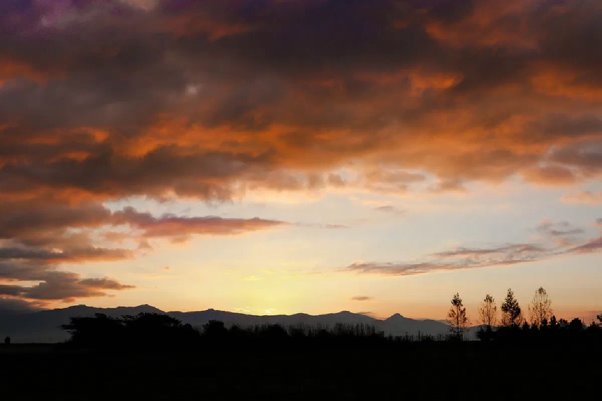 Stunning sunrise with dramatic clouds over Maravatio, Michoacán, Mexico, featuring silhouetted trees and mountains.