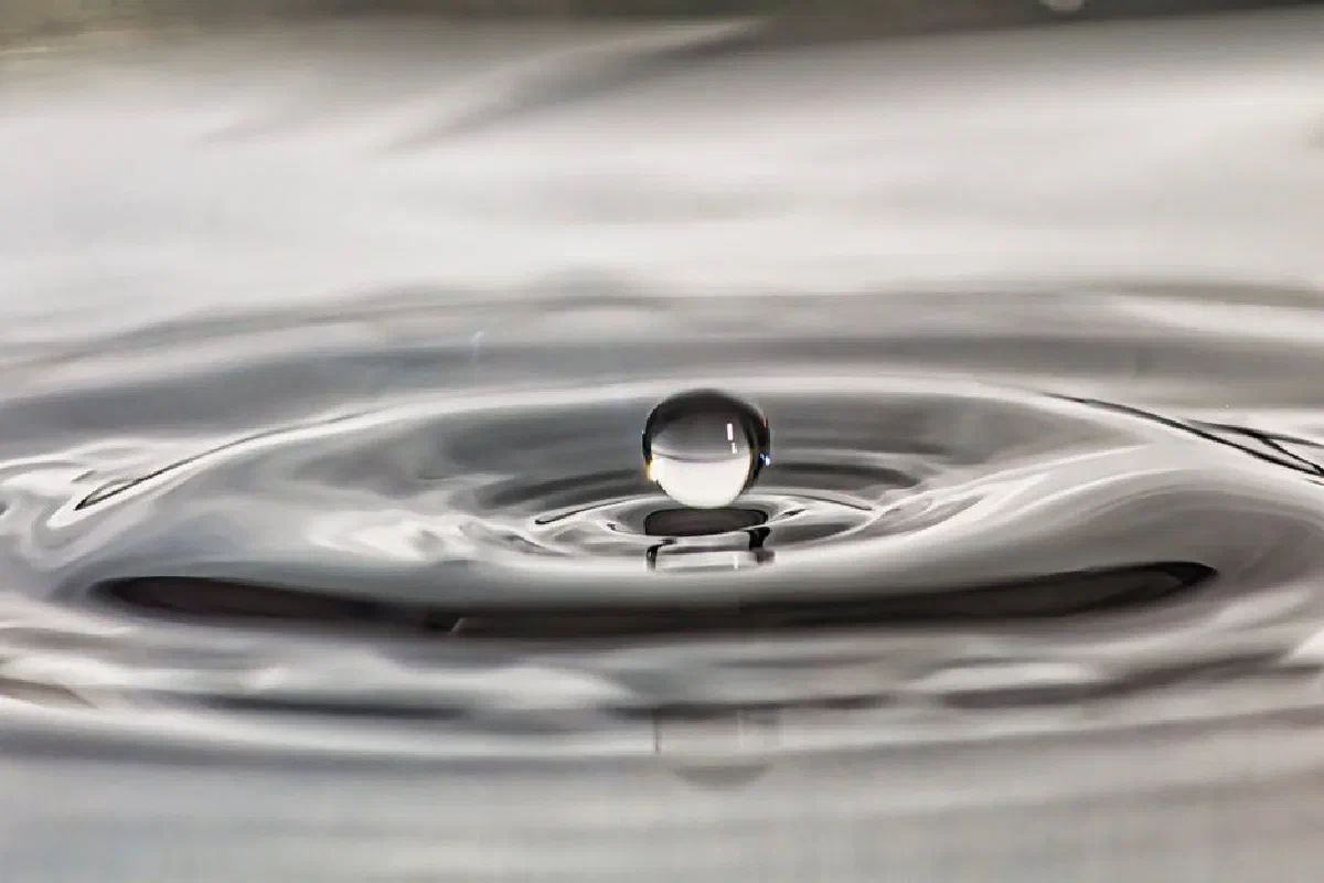 A stunning image of a single water droplet creating ripples on a fluid surface, captured with precision.
