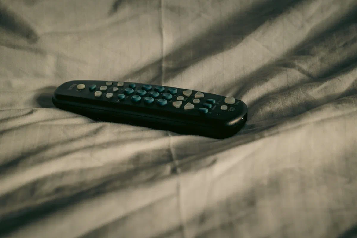 A remote control rests on wrinkled bed sheets, conveying a cozy and relaxed atmosphere.