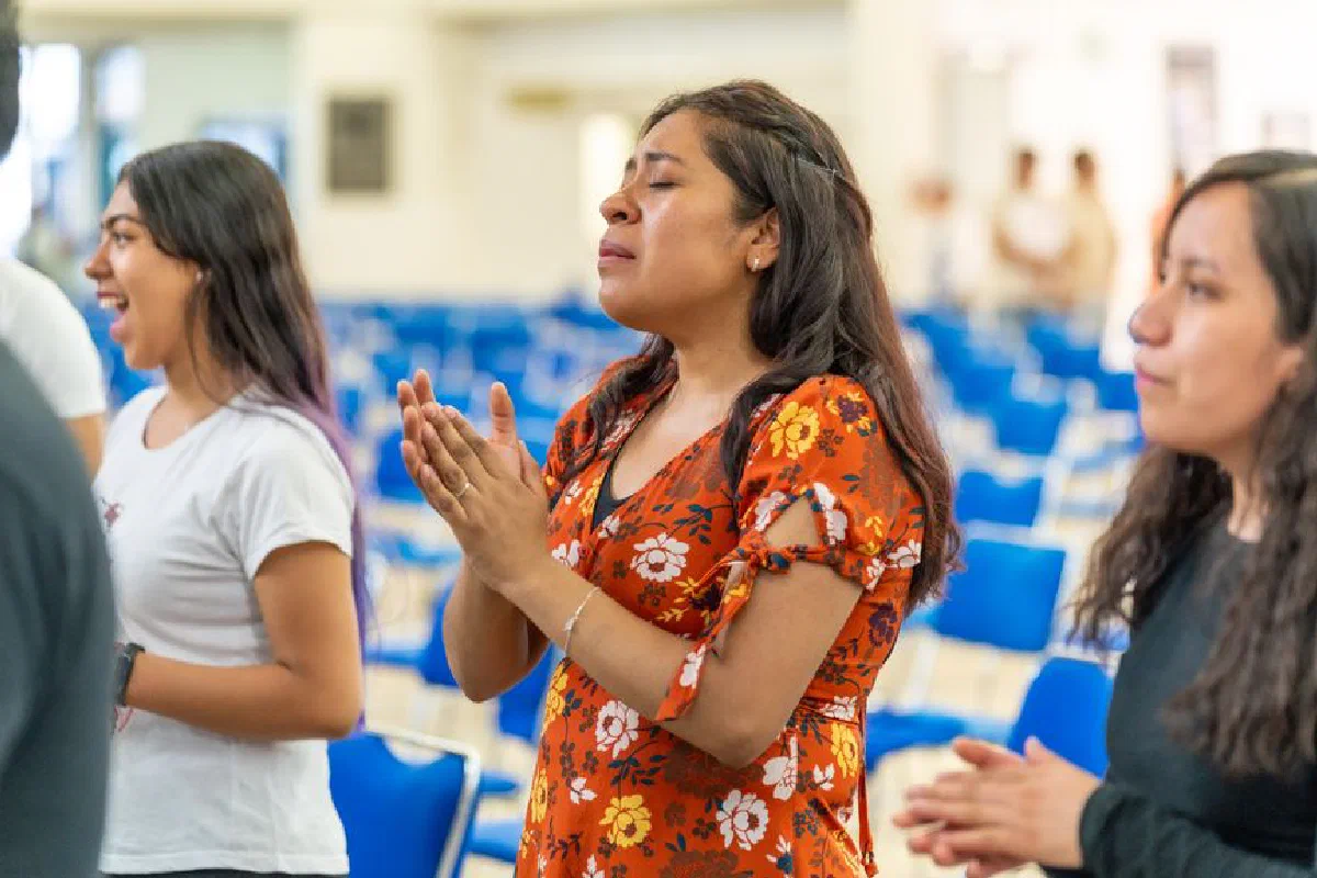 A group of women clapping and praying with closed eyes in a church setting.