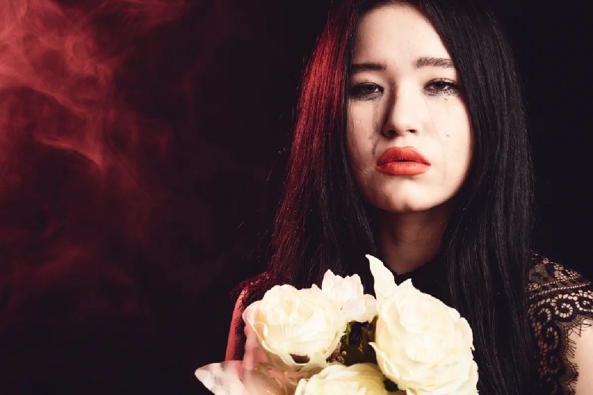 A melancholic portrait of a woman holding white roses against a dark background.