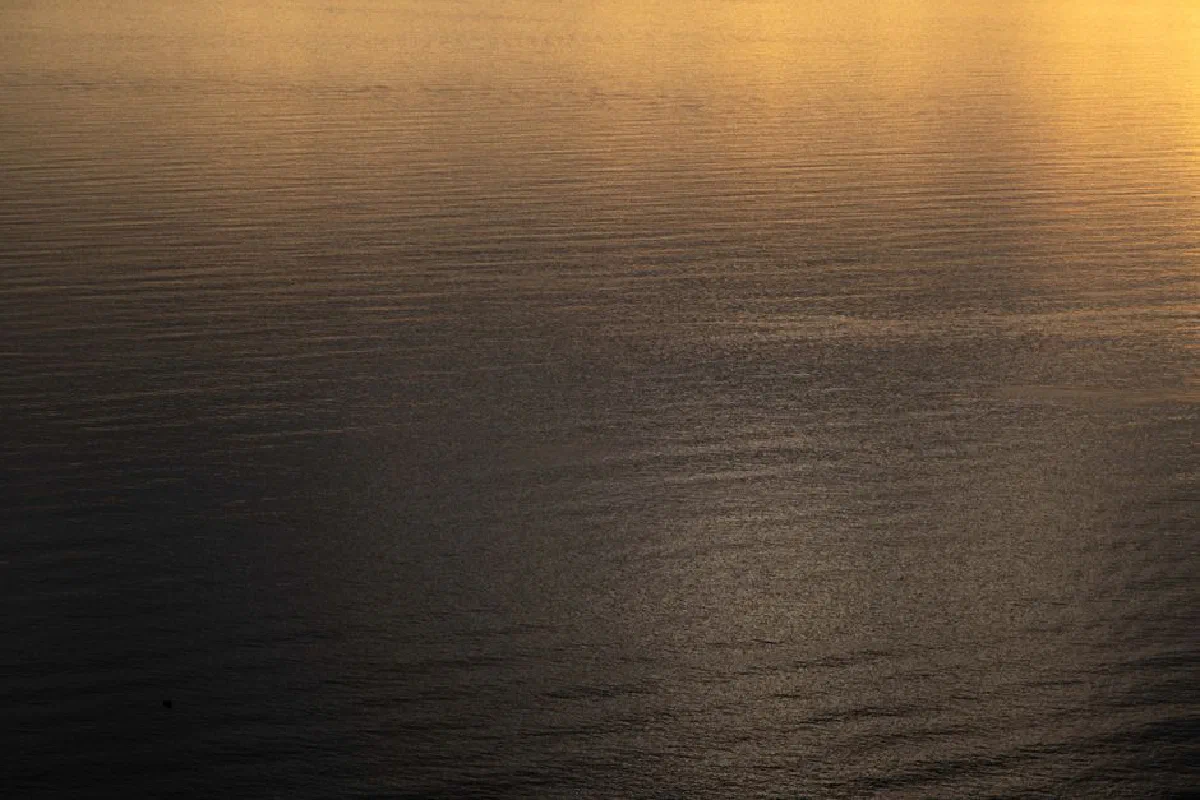 Peaceful view of calm sea reflecting golden sunset light, creating a tranquil and serene atmosphere.