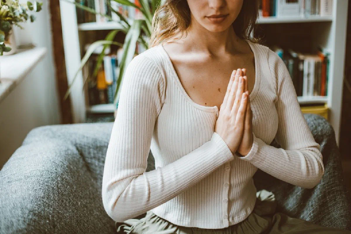 A woman practicing meditation indoors, focusing with hands in prayer position.