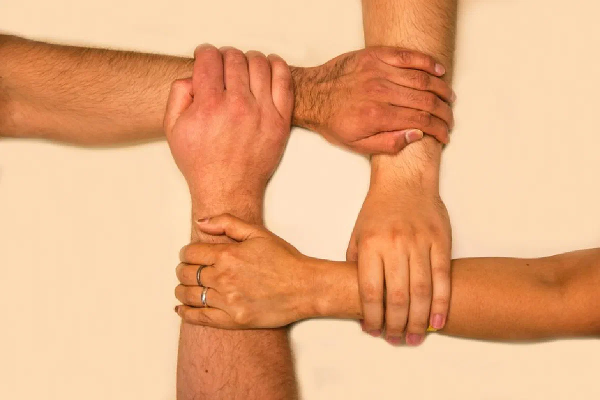 Four hands interlocked, representing unity and teamwork in a symbolic gesture.