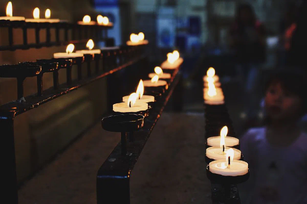 A serene church interior with lit candles on a metal stand, evoking a mood of contemplation.