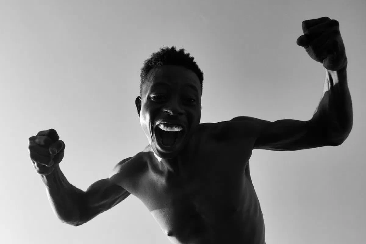 Energetic monochrome portrait of a shirtless man celebrating with fists raised.