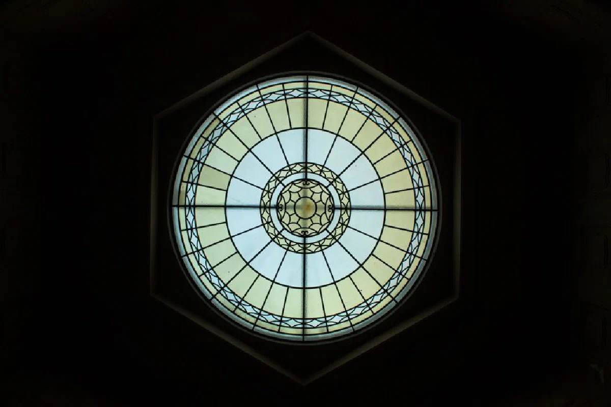 Circular stained glass window inside a church in Bergamo, Italy, showcasing intricate design and lighting.