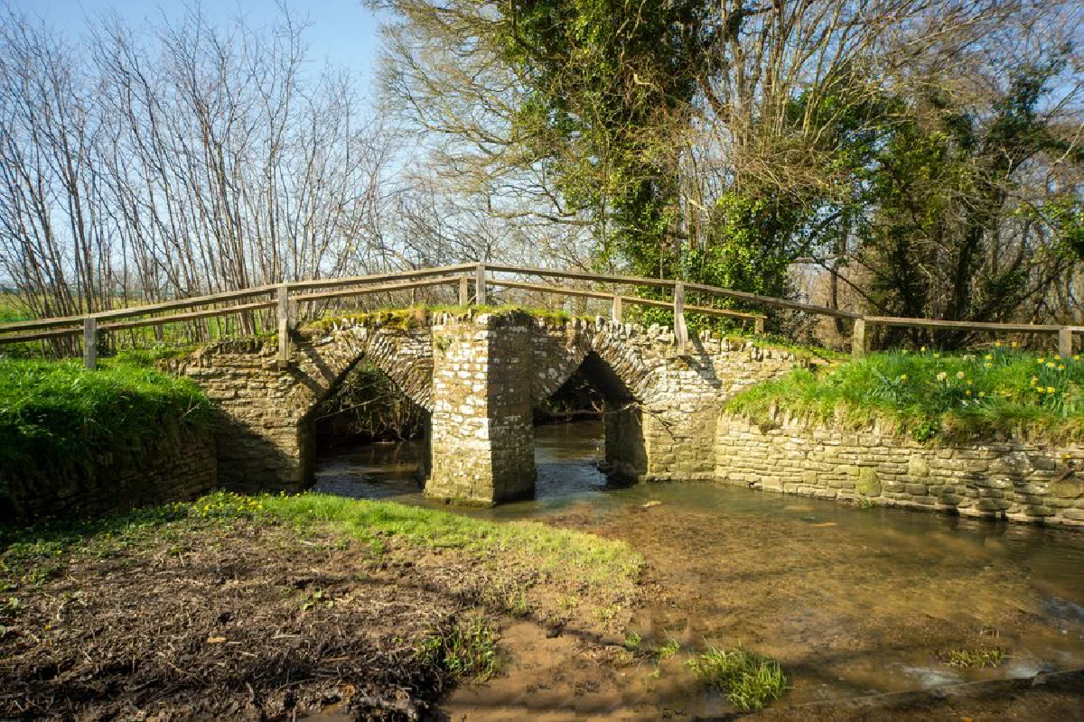 A picturesque medieval stone bridge spanning a serene river on a sunny day.