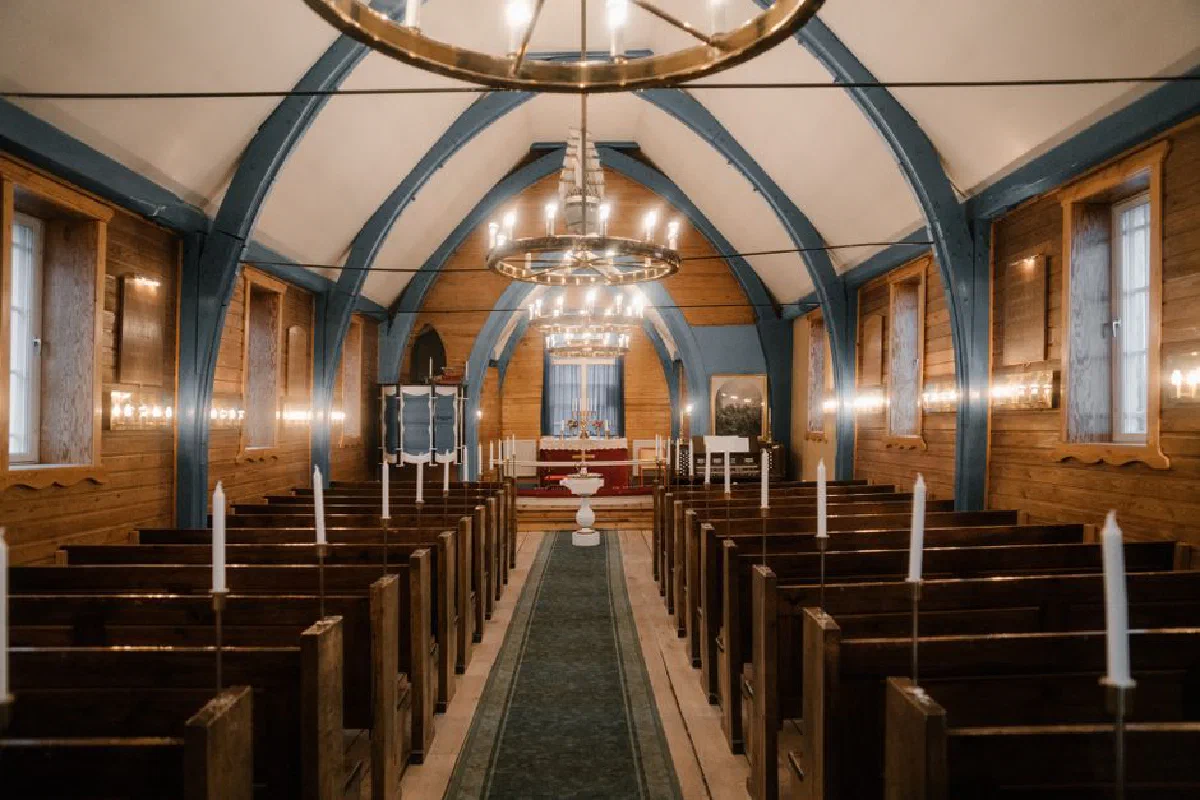 Elegant interior of a wooden church featuring chandeliers and pews, exuding a classic ambiance.