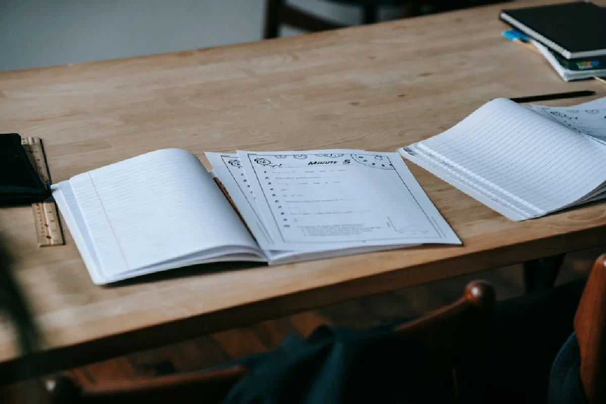 Stationery and opened copybooks with empty sheets placed on wooden desk in light contemporary school