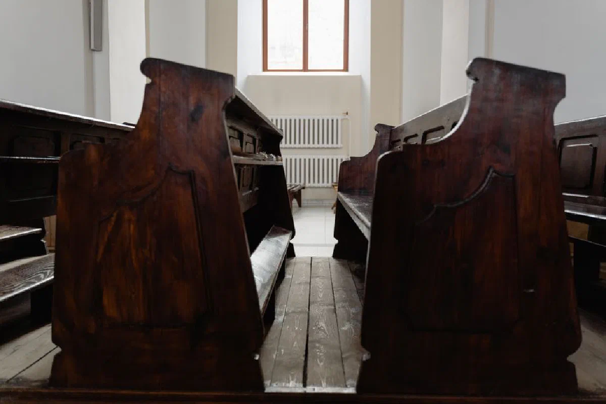 A serene church interior featuring wooden pews and warm natural light streaming through a window.