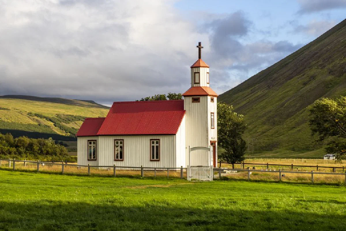 Idyllic red-roofed church in lush Icelandic landscape, surrounded by mountains and greenery.