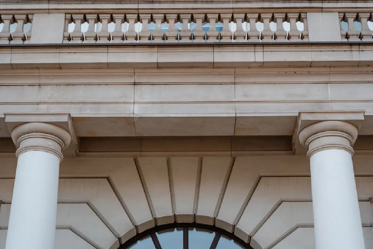 Low angle view of a neoclassical building facade featuring pillars and a balcony in daylight.