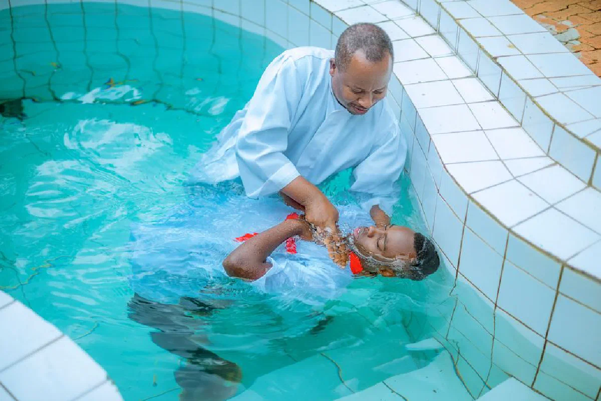 Baptism ceremony in a pool with a minister guiding a young person underwater, symbolizing a spiritual ritual.